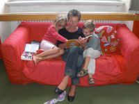 Oma mit Kindern sitzt auf rotem Sofa