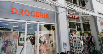 Eingangsbereich der Drogerie mit Parfümwerbung und Sonnenbrillenständer
