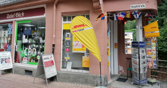 Laden am Eck mit Postkartenaufsteller und CBD Waren im Schaufenster 