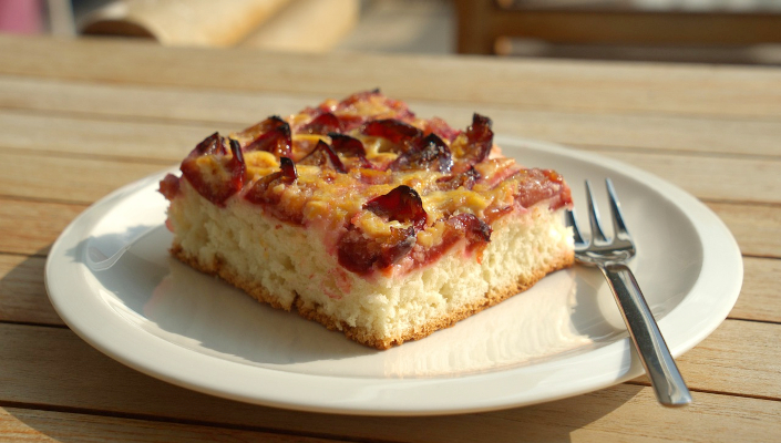 Ein Stück Zwetschgenkuchen auf einem weißen Teller mit Gabel