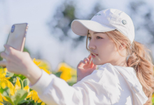 Eine Frau mit weißer Mütze und weißem Pullover macht ein Selfie vor gelben Blumen