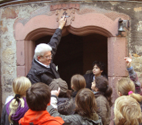Der Stadtführer zeigt auf ein Symbol über einem alten Türrahmen und erklärt den Kindern was dieses zu bedueten hat.