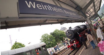 Bahnsteig in Weinheim mit großem Weinheim-Schild und schwarzer historischer Lock im Hintergrund