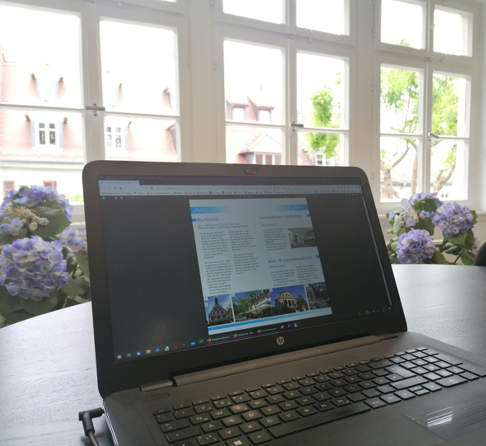 Labtop mit geöffnetem PDF der Broschüre Sehenswert, im Hintergrund Fensterfront mit Hortensien