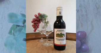 Kleine Flasche Rotwein mit Weingläsern und Weintrauben auf einem Holzfass