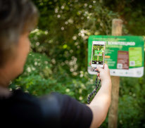Eine Frau scannt mit einem Smartphone den QR-Code auf einem Schild