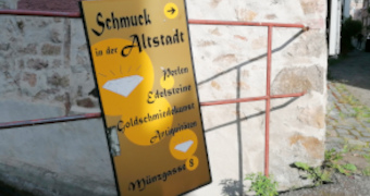 Goldenes Schild mit Angeboten an einem Zaun vor Fachwerkhaus