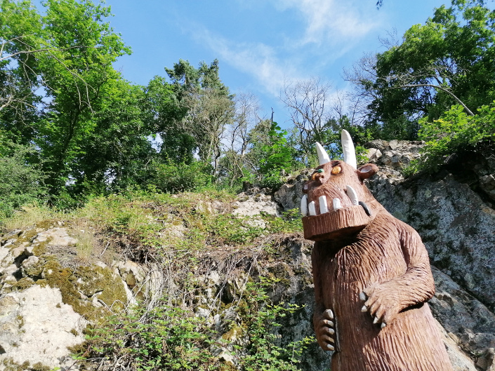 Grüffelo-Statue aus Holz vor Felswand