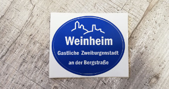 Blauer ovaler Aufkleber mit weißer Schrift Weinheim Gastliche Zweiburgenstadt an der Bergstraße.