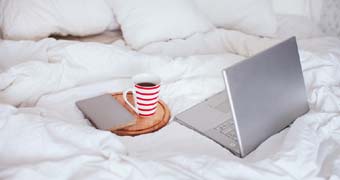 Silberner Labtop und Teetasse auf einem Bett