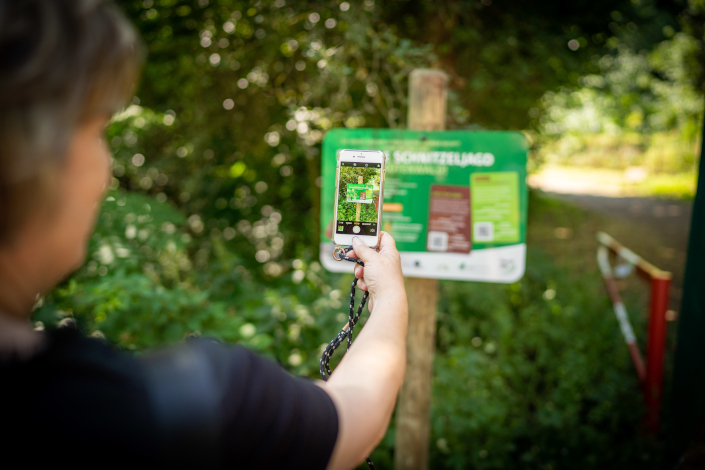 Eine Frau scannt mit ihrem Smartphone den QR-Code an einem Schild